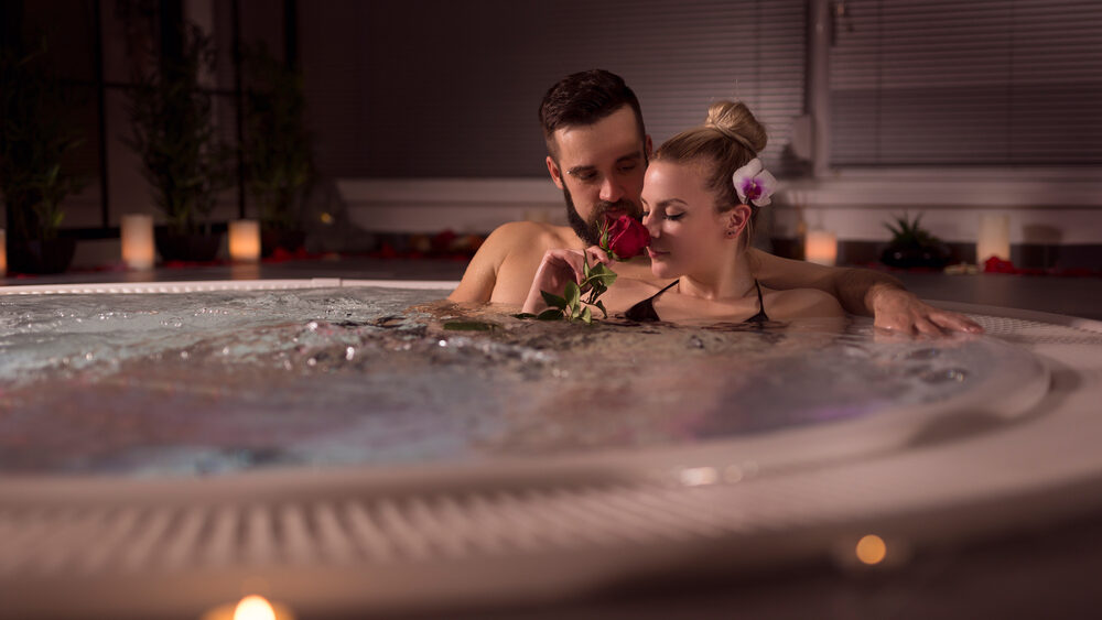 Couple relaxing together in a private hot tub with candles, rose, and soft lighting for a romantic setting